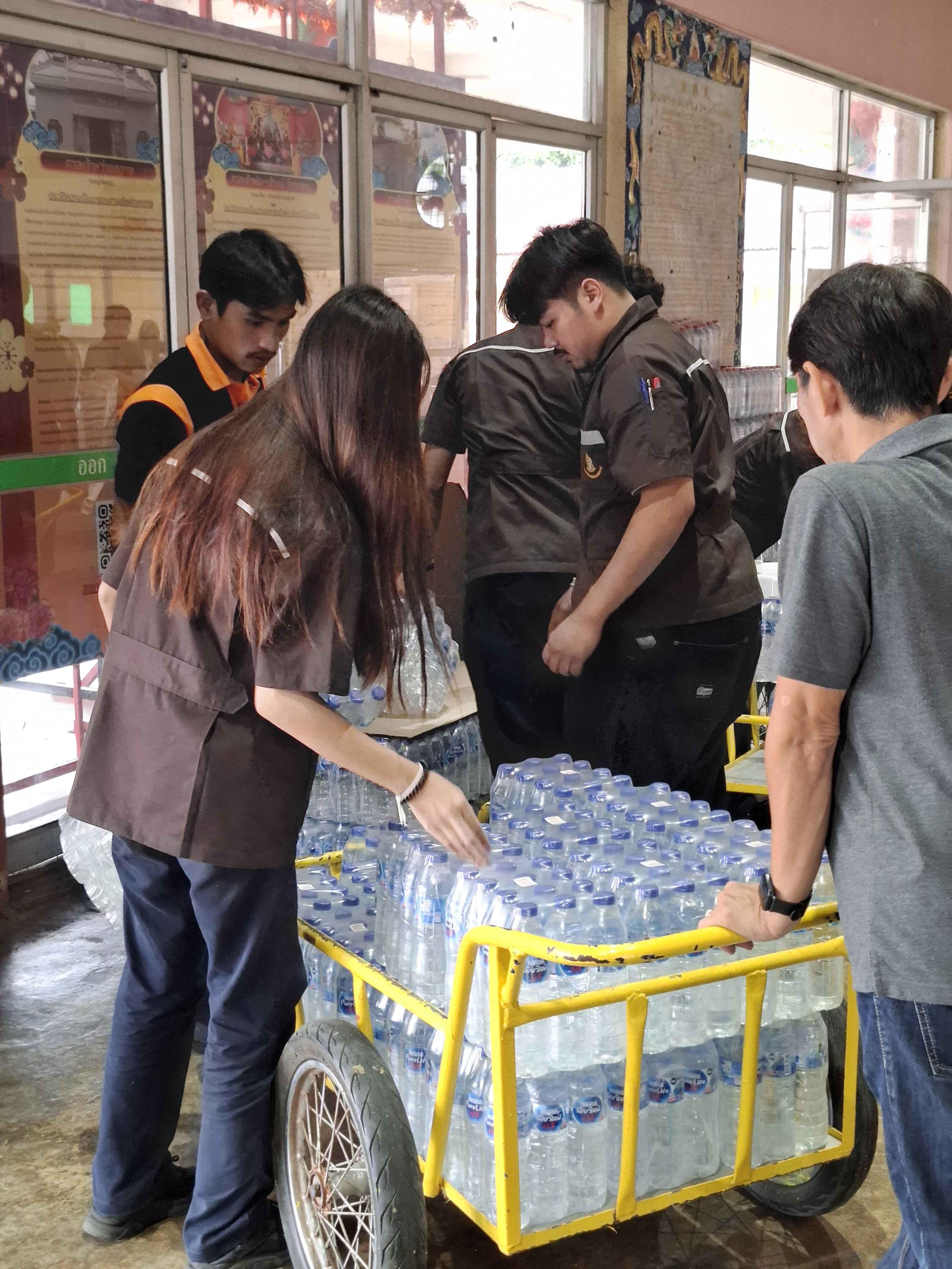 คณะทำงานช่วยกันขนย้ายและจัดวางน้ำดื่มบรรจุขวดลงบนรถเข็น